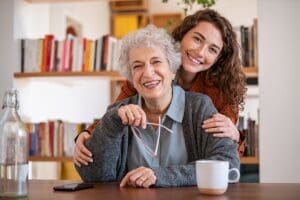 Young,Woman,Embracing,Senior,Mother,At,Home,And,Looking,At