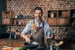 Handsome,Young,Man,With,Apron,Frying,Vegetables,For,Pasta