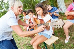 Teacher,Helps,Children,Learn,To,Play,Guitar,In,Class,At