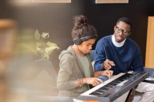 Cute,Diligent,Schoolgirl,Pushing,Keys,Of,Piano,Keyboard,While,Teacher