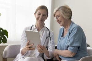 Positive,Practitioner,Doctor,Showing,Tablet,Screen,To,Elder,70s,Patient