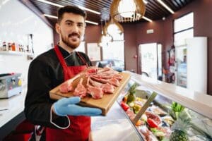 Young,Butcher,Holding,Raw,Lamb,Ribs,In,A,Butcher,Shop